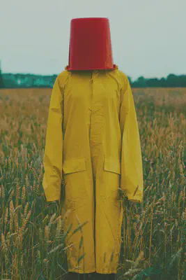 Person in Yellow in Field with Bucket on Head